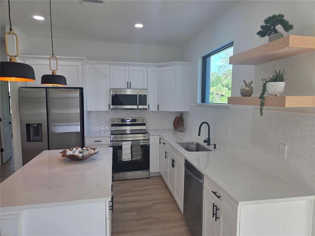 A modern kitchen features white cabinets, stainless steel appliances, quartz countertops, and a central island — 2074 RIBBON TERRACE, NORTH PORT, FL
