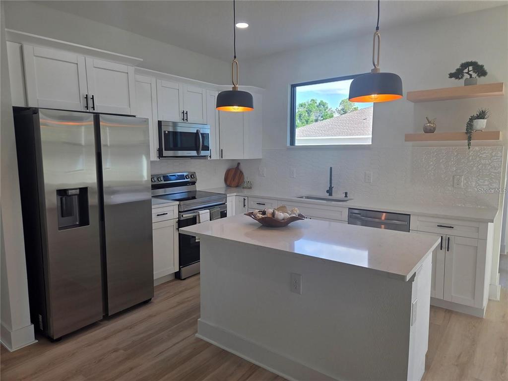 A modern kitchen features white cabinets, stainless steel appliances, a center island, and floating shelves — 2074 RIBBON TERRACE, NORTH PORT, FL