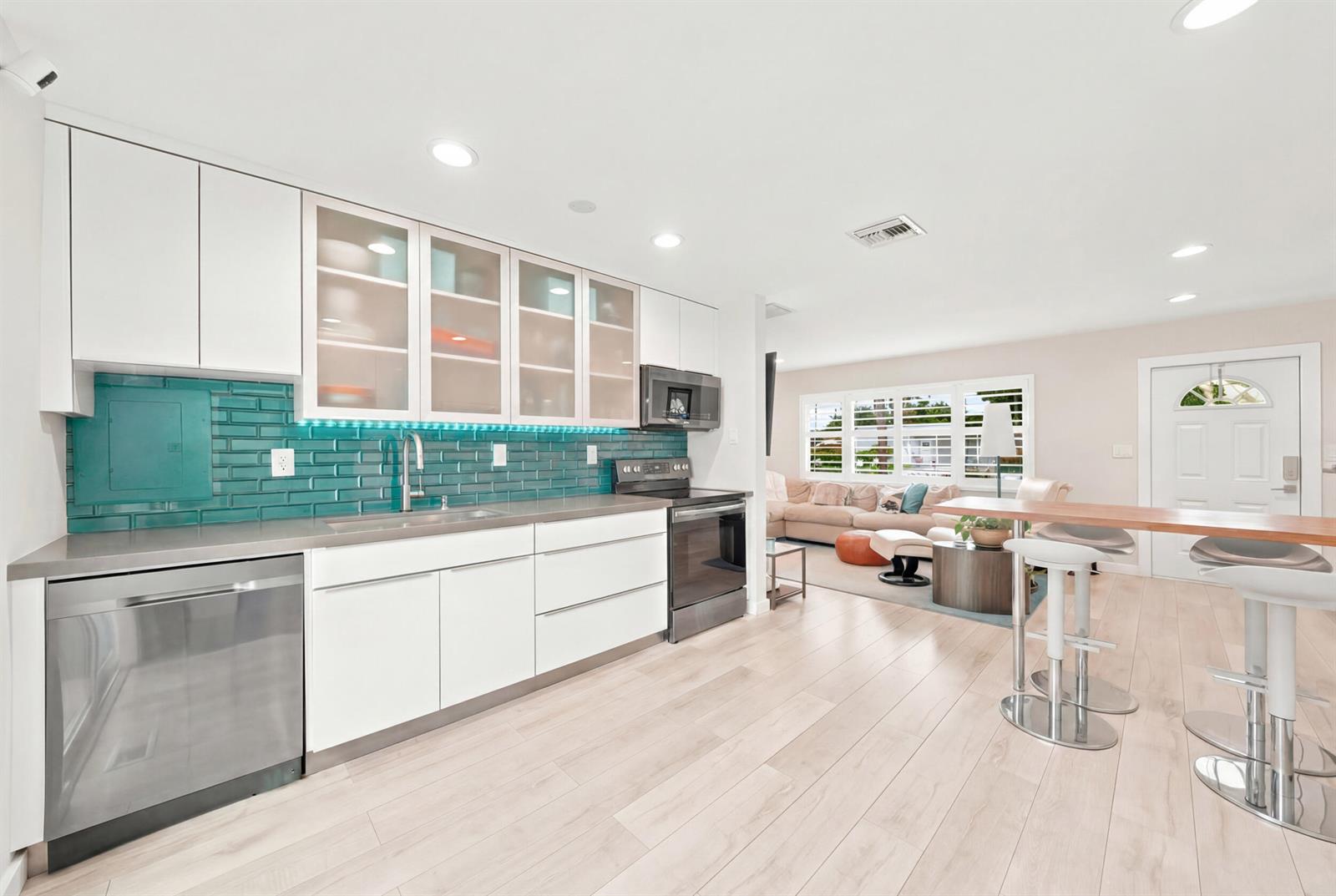 A modern kitchen with white cabinets, teal subway tile backsplash, and a breakfast bar — 3140 NE 12th Avenue, Pompano Beach FL 33064, POMPANO BEACH, FL