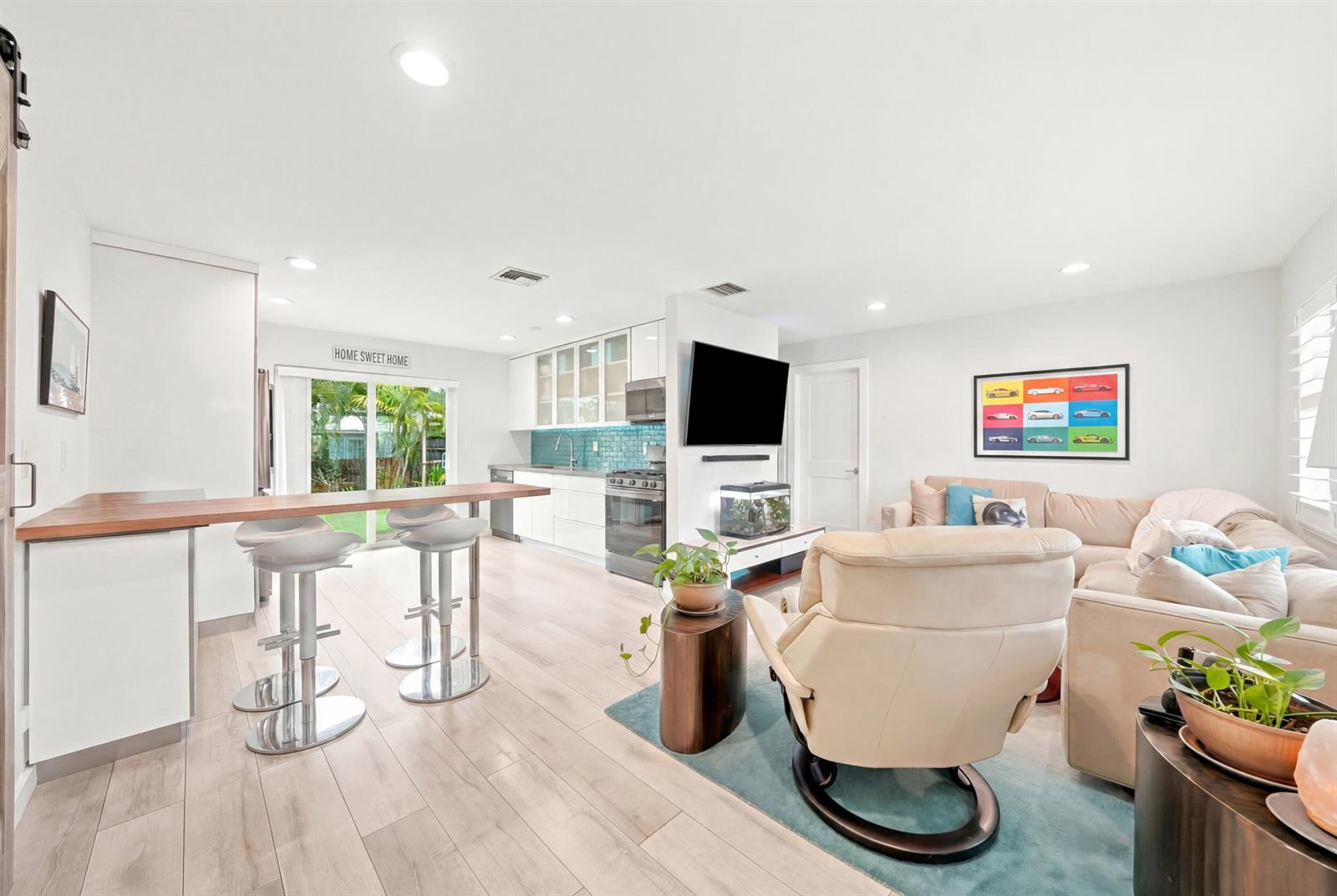 An open-concept living room and kitchen featuring light wood floors, white cabinetry, and bar seating — 3140 NE 12th Avenue, Pompano Beach FL 33064, POMPANO BEACH, FL