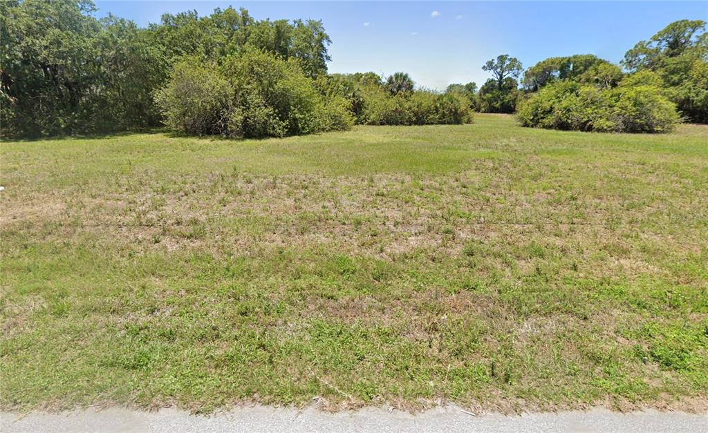 A vacant, grassy lot is bordered by trees and shrubs under a clear blue sky — 109 WAYNE ROAD, ROTONDA WEST, FL