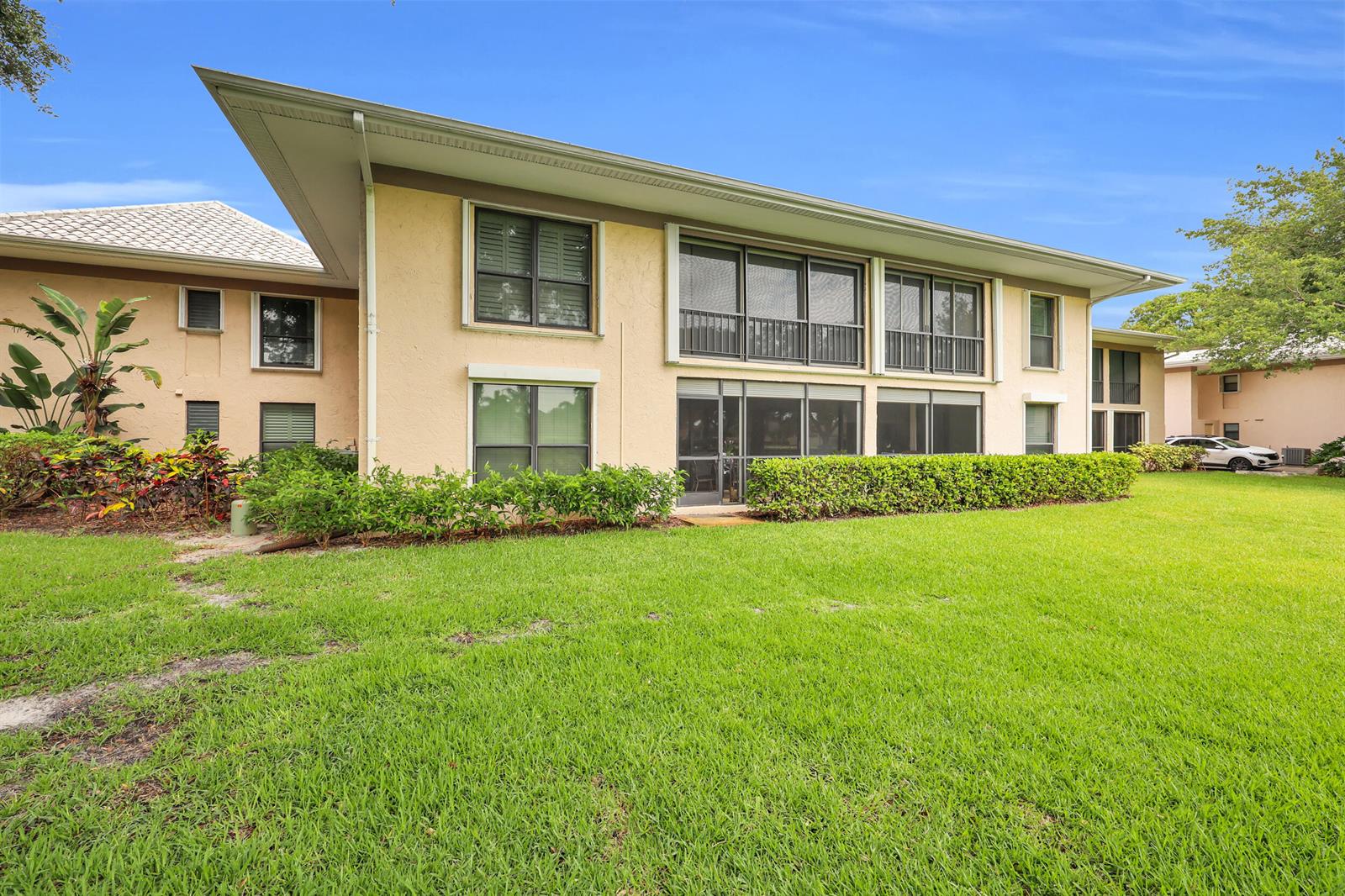 A two-story apartment building with beige stucco walls, screened balconies, and a large grassy lawn — 10 SE Turtle Creek Drive Unit B, Tequesta FL 33469, TEQUESTA, FL