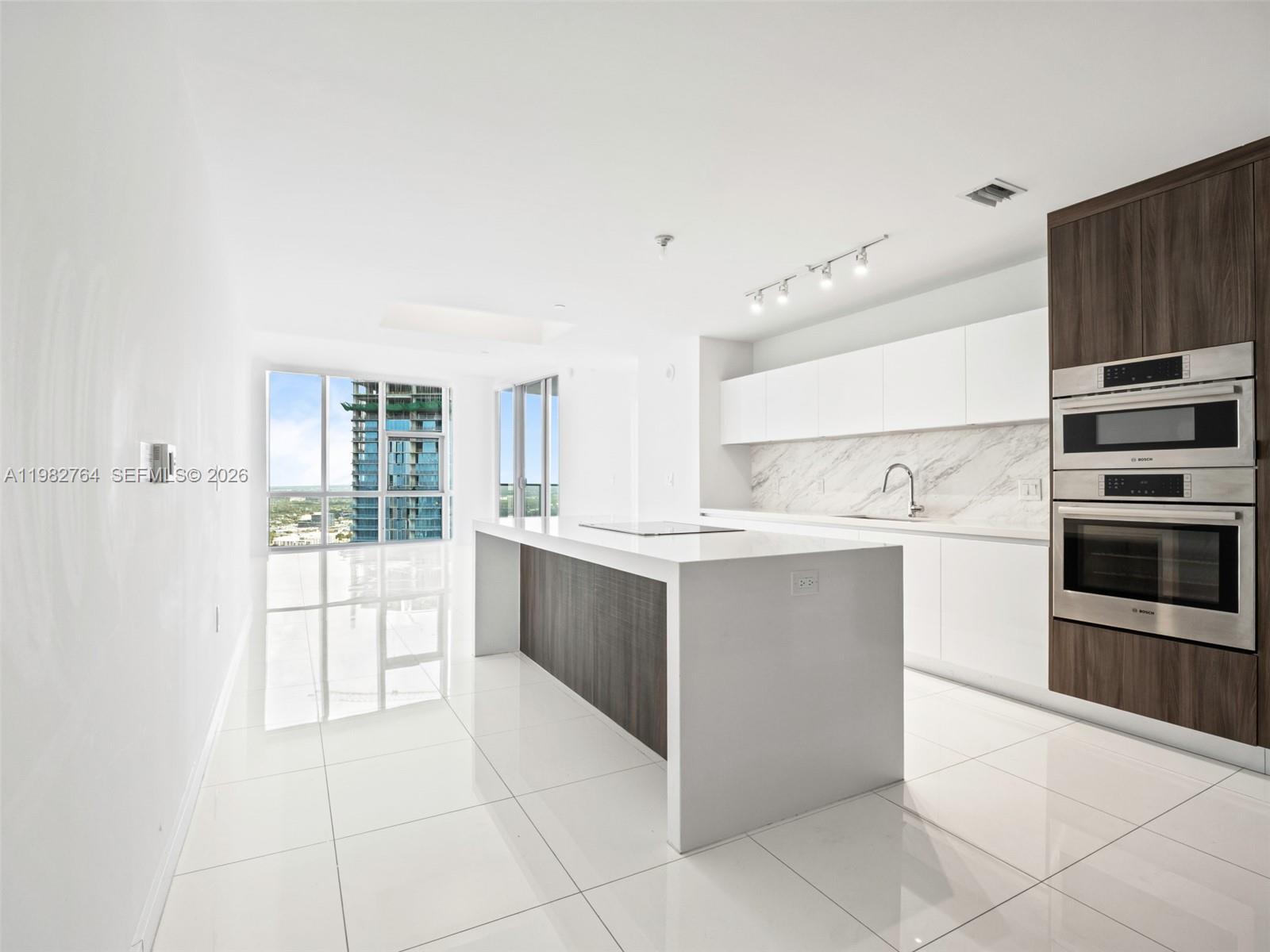 A modern kitchen features a white island, marble backsplash, and stainless steel wall ovens — 851 NE 1st Ave # 4801, Miami FL 33132, MIAMI, FL