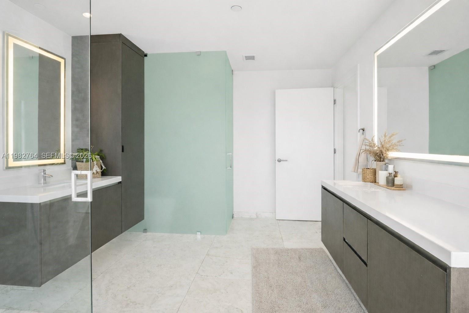 A modern bathroom features dual vanities with dark cabinetry, white countertops, and a glass-enclosed shower — 851 NE 1st Ave # 4801, Miami FL 33132, MIAMI, FL