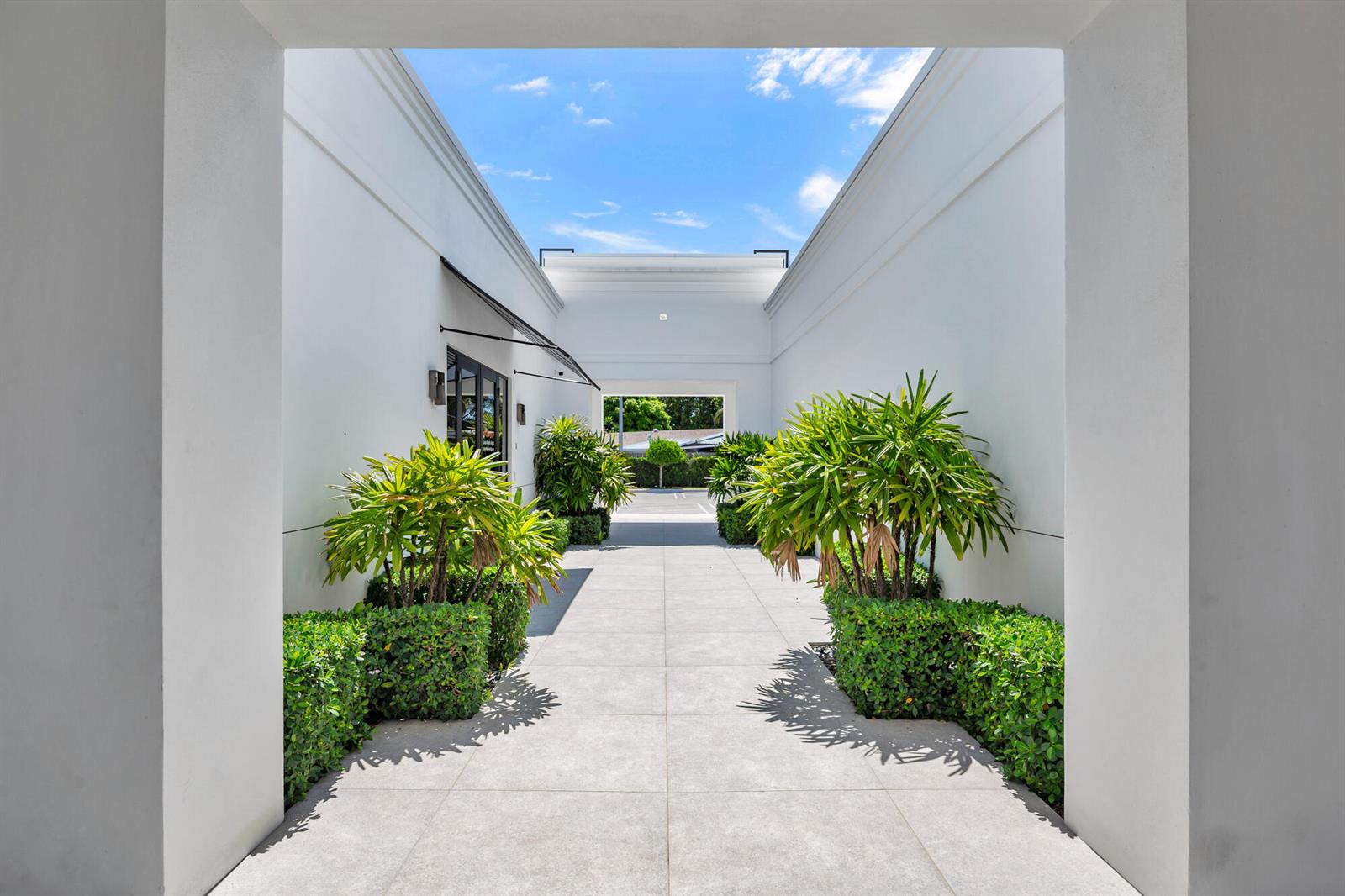 An outdoor walkway with white walls, tiled flooring, and potted plants leads to a parking area — 6500 S Dixie Highway # C, West Palm Beach FL 33405, WEST PALM BEACH, FL