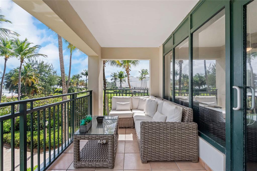 A balcony with wicker sectional seating, a glass-top table, and a view of palm trees — 6100 RIO MAR UNIT 829899, RIO GRANDE, PR