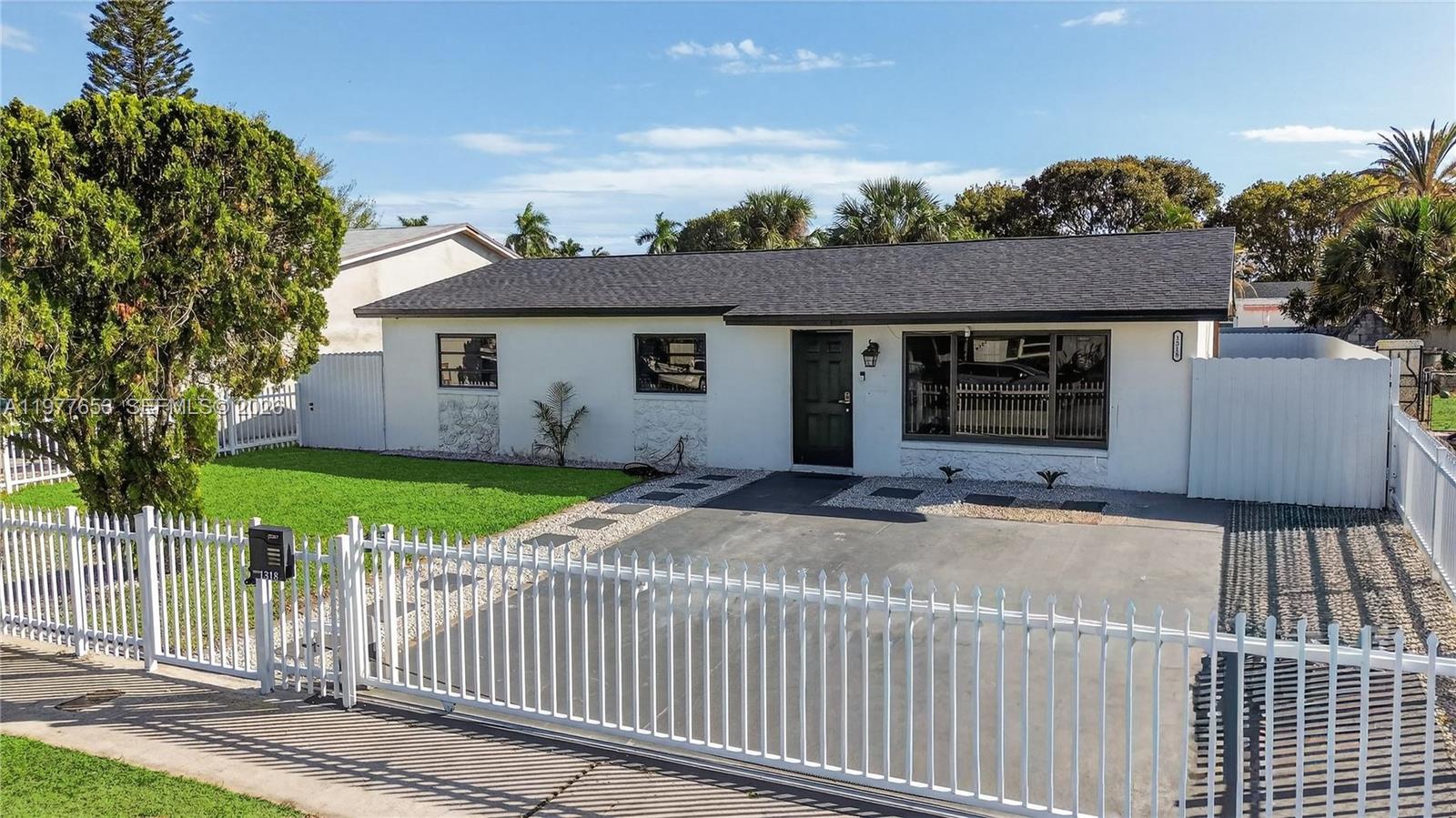 A single-story white house with a dark roof sits behind a white metal fence — 1318 13th St, West Palm Beach FL 33401, WEST PALM BEACH, FL
