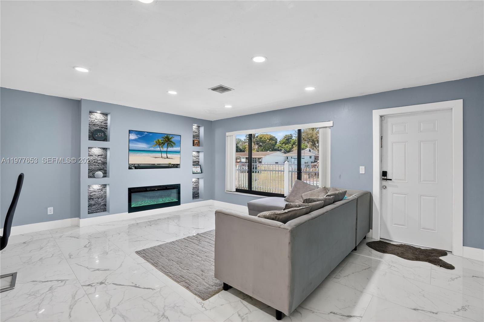 A living room features light blue walls, marble-look tile floors, a fireplace, and built-in shelving — 1318 13th St, West Palm Beach FL 33401, WEST PALM BEACH, FL