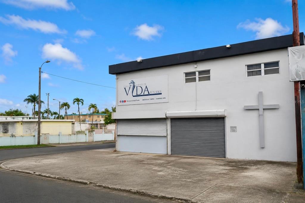 A white commercial building with a cross on the wall and two metal roll-down doors — 22 URB. RIVERVIEW AA1, CALLE 22, BAYAMON, PR