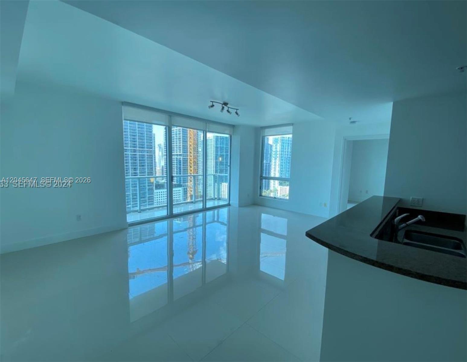 An empty living room features white tile floors, floor-to-ceiling windows, and a kitchen counter — 300 S Biscayne Blvd # 2302, Miami FL 33131, MIAMI, FL
