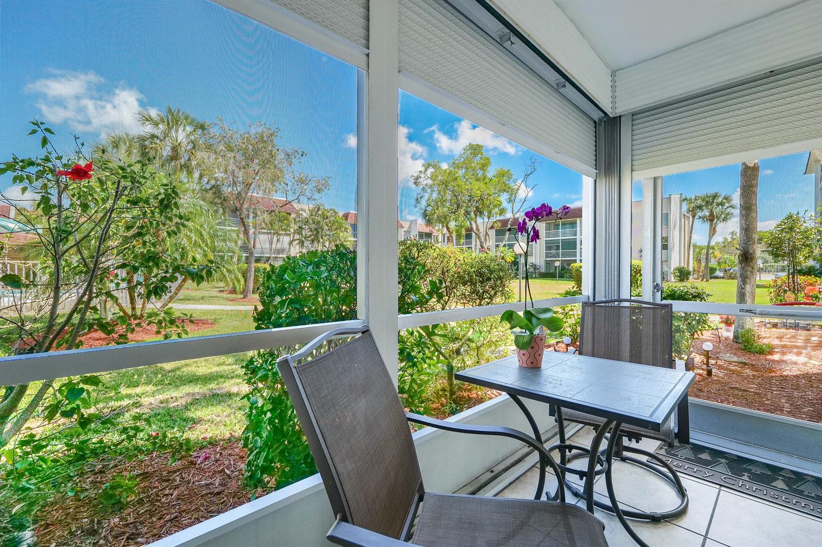 A screened-in patio features a small table, two chairs, and views of a landscaped courtyard — 3531 Inverrary Drive # 105, Lauderhill FL 33319, LAUDERHILL, FL