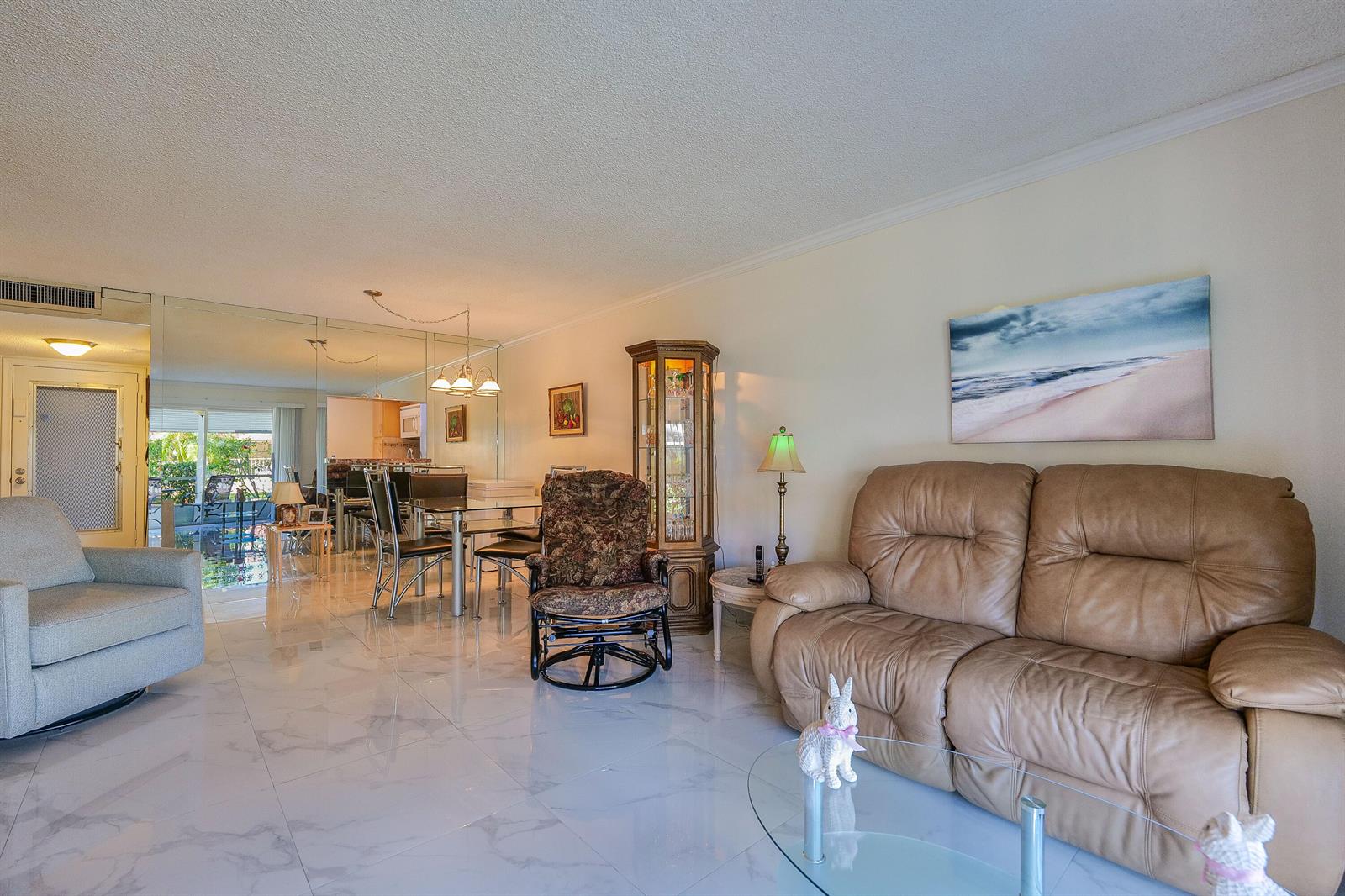 A living room with a tan leather sofa, a floral rocker, and white marble-style flooring — 3531 Inverrary Drive # 105, Lauderhill FL 33319, LAUDERHILL, FL