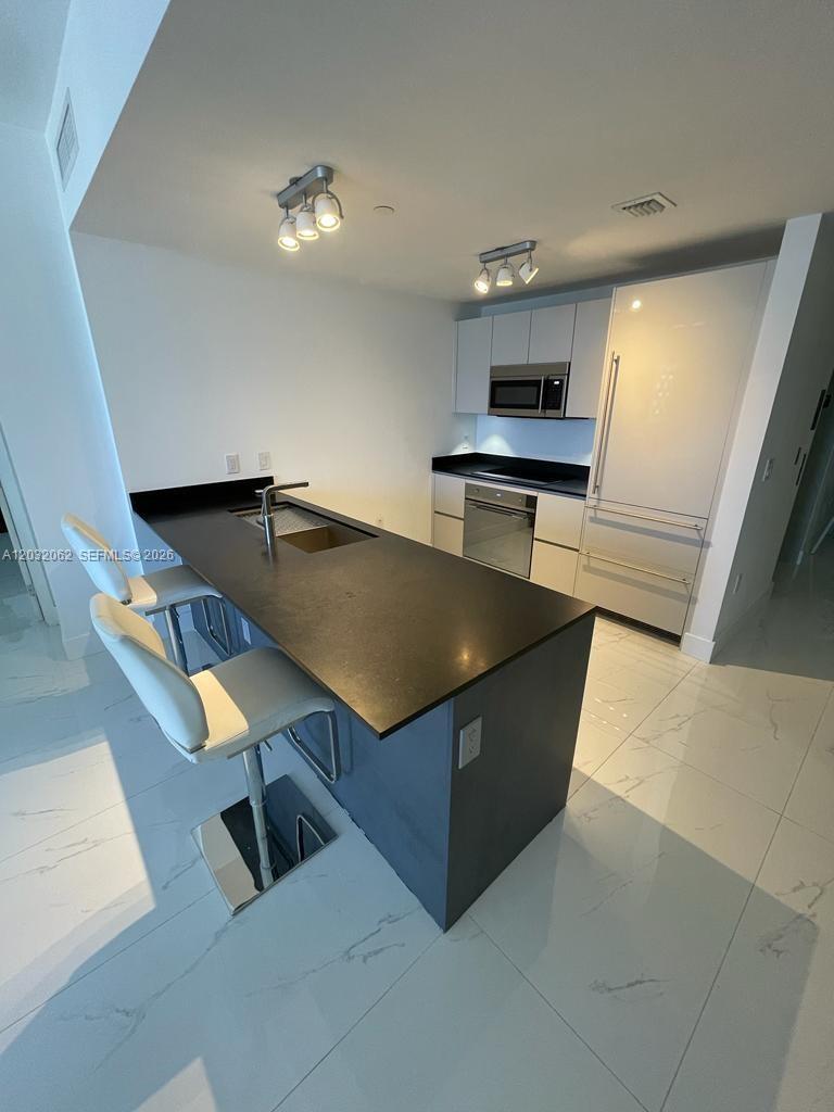 A modern kitchen features a black island, white cabinetry, stainless steel appliances, and tile flooring — 1010 Brickell Ave # 2704, Miami FL 33131, MIAMI, FL
