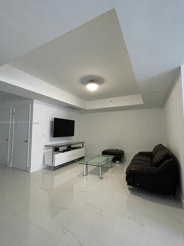 A living room features white tile floors, a black leather sofa, and a wall-mounted television — 1010 Brickell Ave # 2704, Miami FL 33131, MIAMI, FL