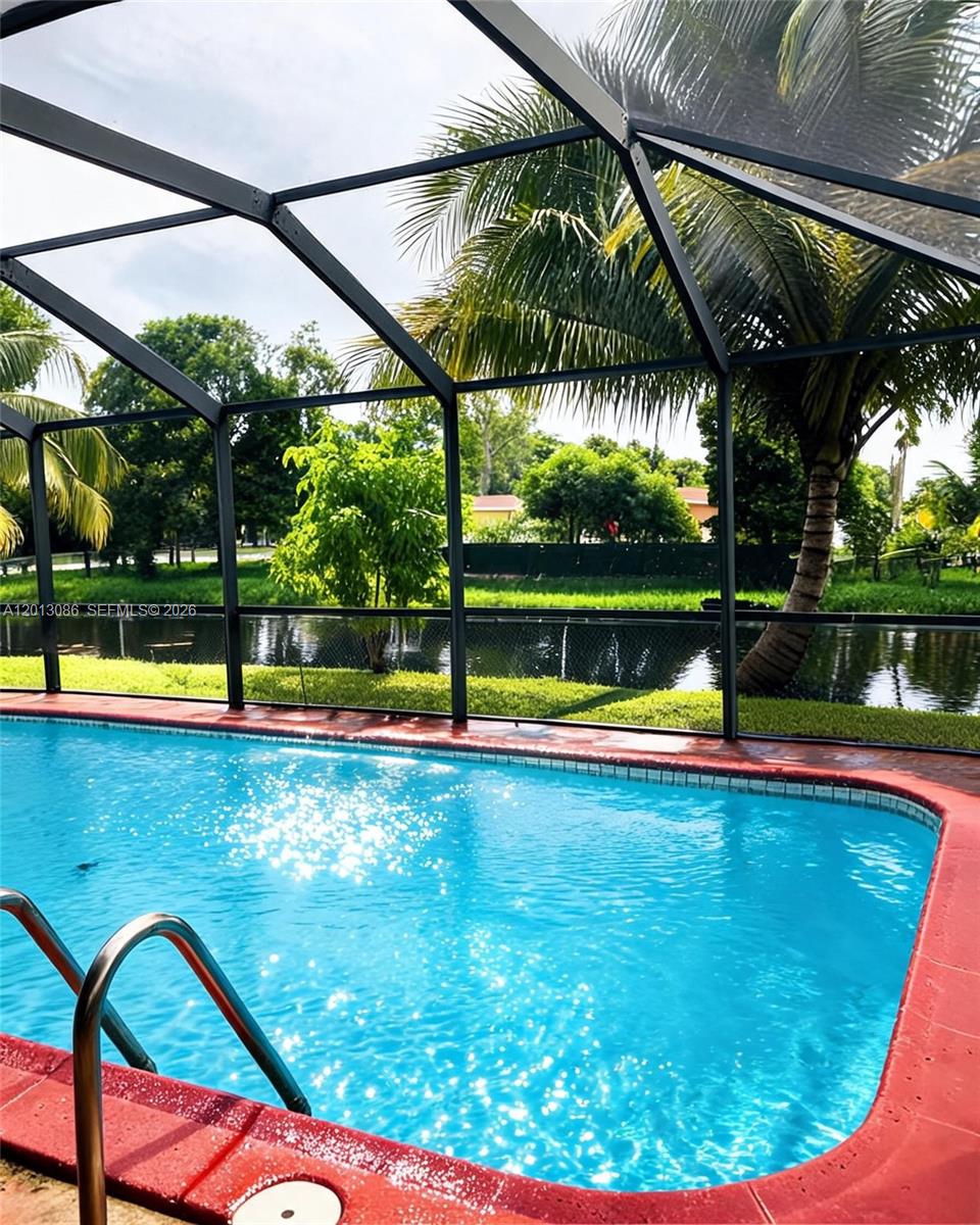 A swimming pool with a red deck is enclosed by a screen cage overlooking a canal — 2160 NW 82nd Ter, Sunrise FL 33322, SUNRISE, FL