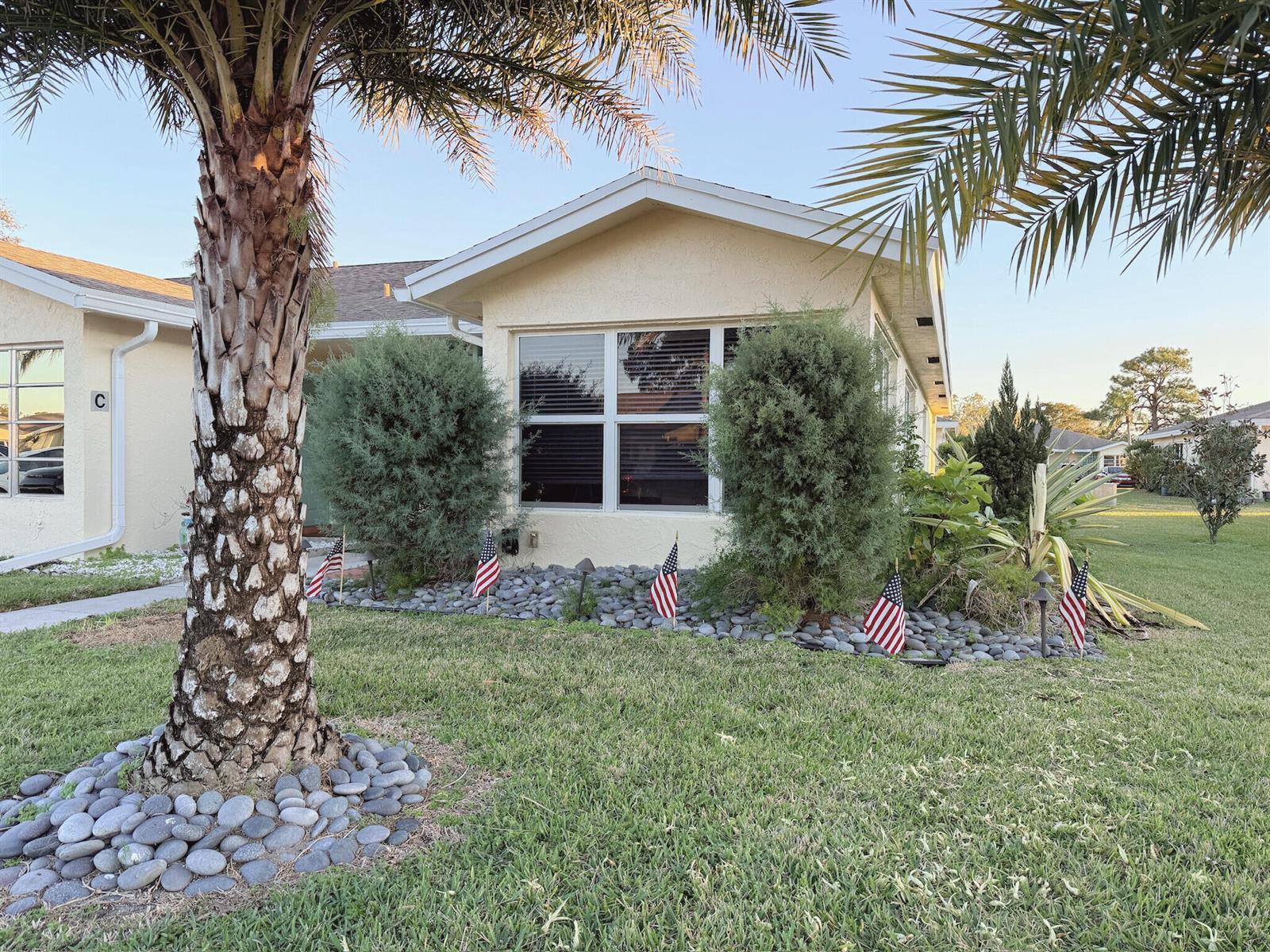 A single-story house with a palm tree, rock landscaping, and American flags in the yard — 5301 Lakefront Boulevard # D, Delray Beach FL 33484, DELRAY BEACH, FL