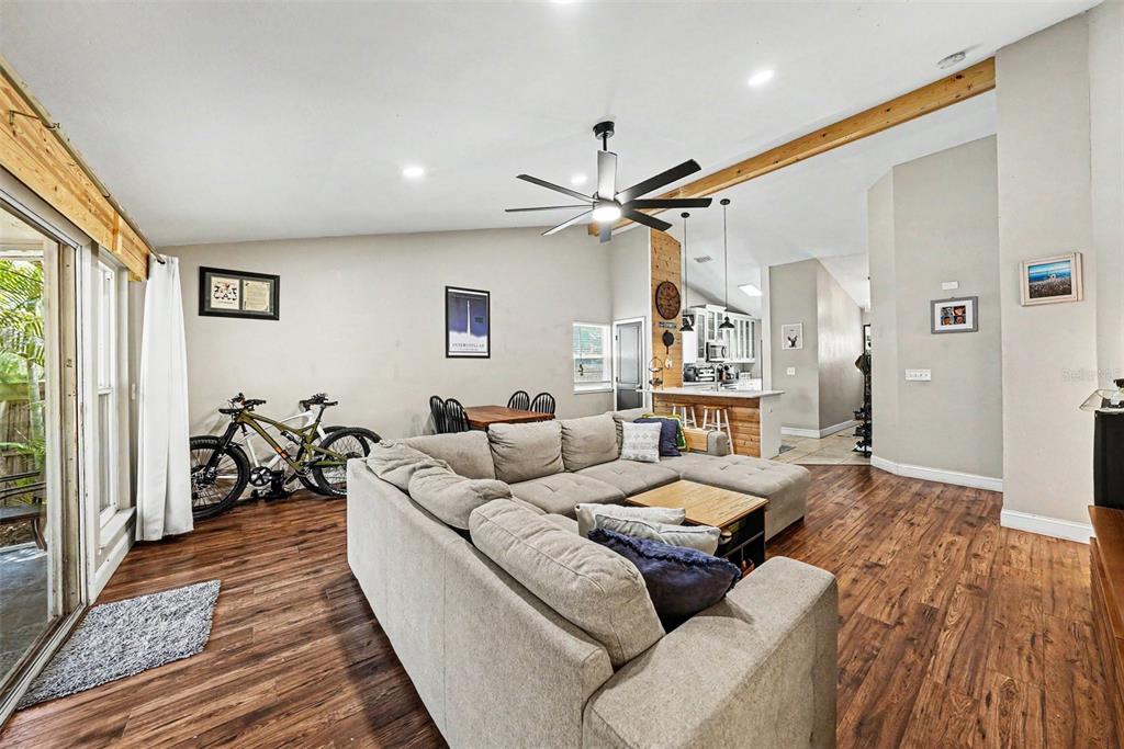 A living room with wood-look flooring, a large sectional sofa, and an open kitchen area — 6209 INTERBAY BOULEVARD, TAMPA, FL