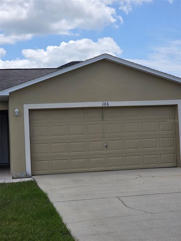 A beige garage door with the number 106 above it sits in front of a driveway — 106 HERRING LANE, POINCIANA, FL