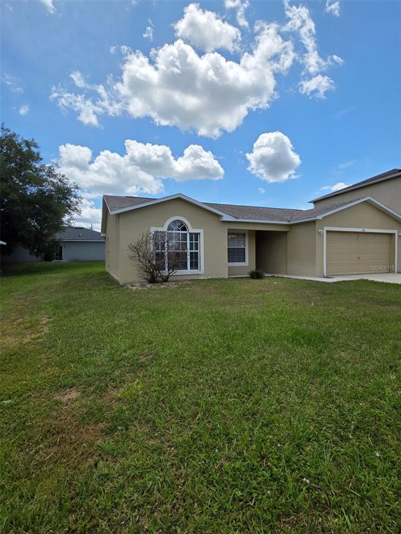 A single-story tan house with a front-facing garage and an arched window under a blue sky — 106 HERRING LANE, POINCIANA, FL