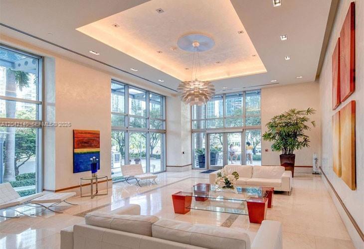 A bright, modern lobby features high ceilings, large windows, white sofas, and a central chandelier — 1050 Brickell Ave # 416, Miami FL 33131, MIAMI, FL