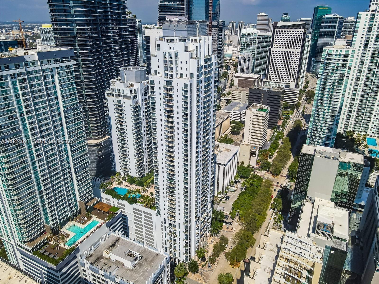 An aerial view of a tall white residential skyscraper surrounded by other urban high-rise buildings — 1050 Brickell Ave # 416, Miami FL 33131, MIAMI, FL
