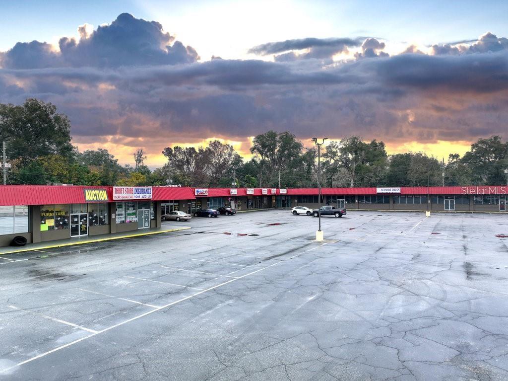 A low-rise commercial strip mall with a large parking lot under a dramatic sunset sky — 3410 NE JACKSONVILLE ROAD, OCALA, FL