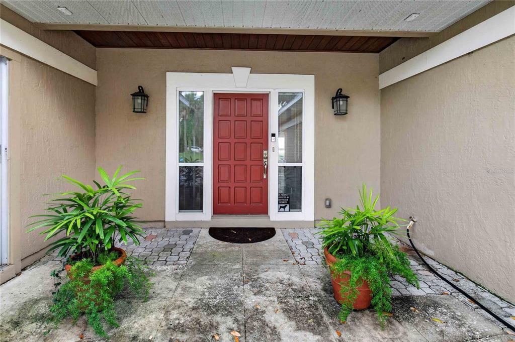 A red front door is centered between two sidelight windows on a concrete porch — 5616 TRIMBLE PARK ROAD, MOUNT DORA, FL