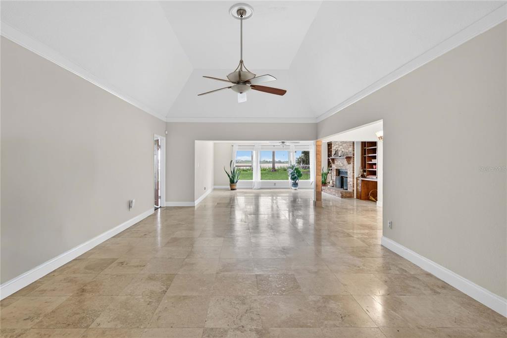 A spacious living area features light-colored tile flooring, a vaulted ceiling, and a brick fireplace — 5616 TRIMBLE PARK ROAD, MOUNT DORA, FL