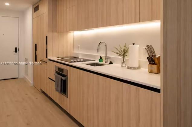 A modern kitchen features light wood cabinetry, white countertops, and integrated appliances — 225 N Miami Ave # 2008, Miami FL 33128, MIAMI, FL