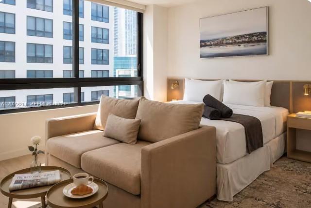 A hotel-style bedroom features a beige sofa, a queen bed, and large windows overlooking buildings — 225 N Miami Ave # 2008, Miami FL 33128, MIAMI, FL