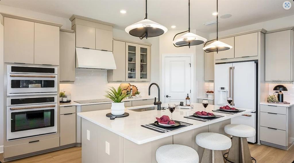 A modern kitchen features light-colored cabinetry, a large central island, and stainless steel appliances — 26201 ATRANI DRIVE, ENGLEWOOD, FL