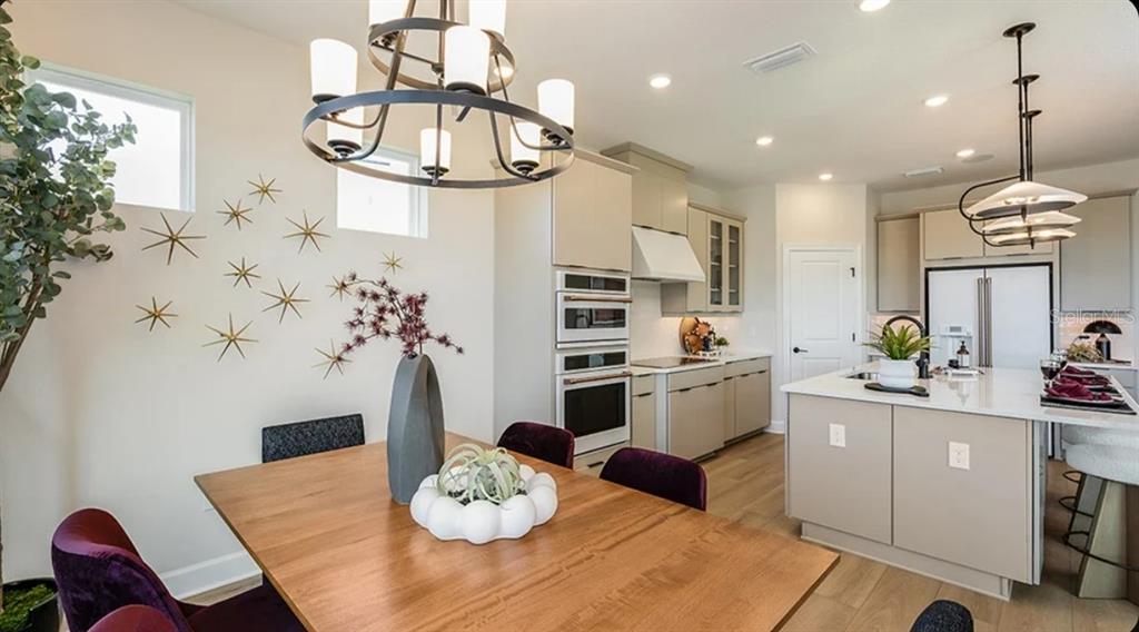 A modern kitchen and dining area with light cabinets, wood flooring, and a large island — 26201 ATRANI DRIVE, ENGLEWOOD, FL