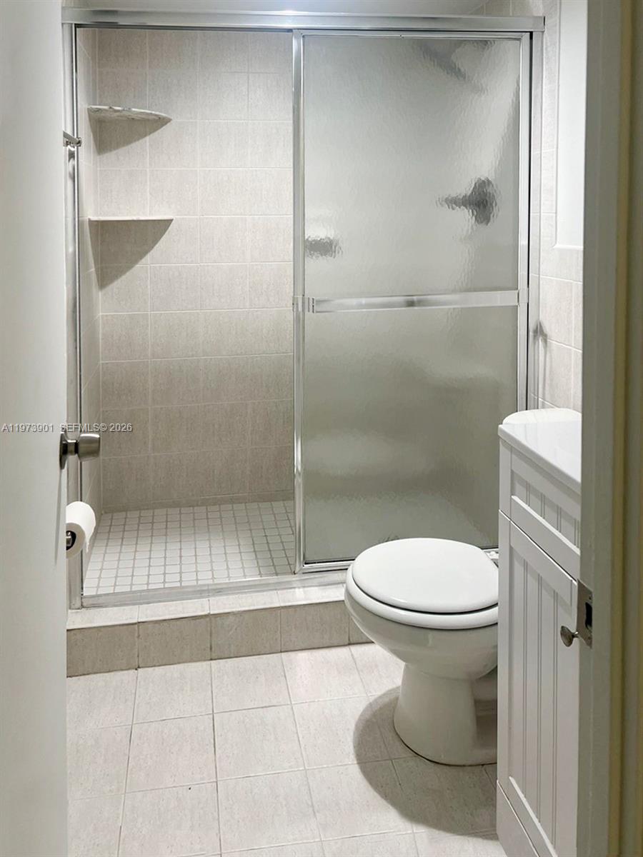 A bathroom features a tiled shower with a glass door, a toilet, and a vanity — 447 NE 195th St # 217, Miami FL 33179, MIAMI, FL