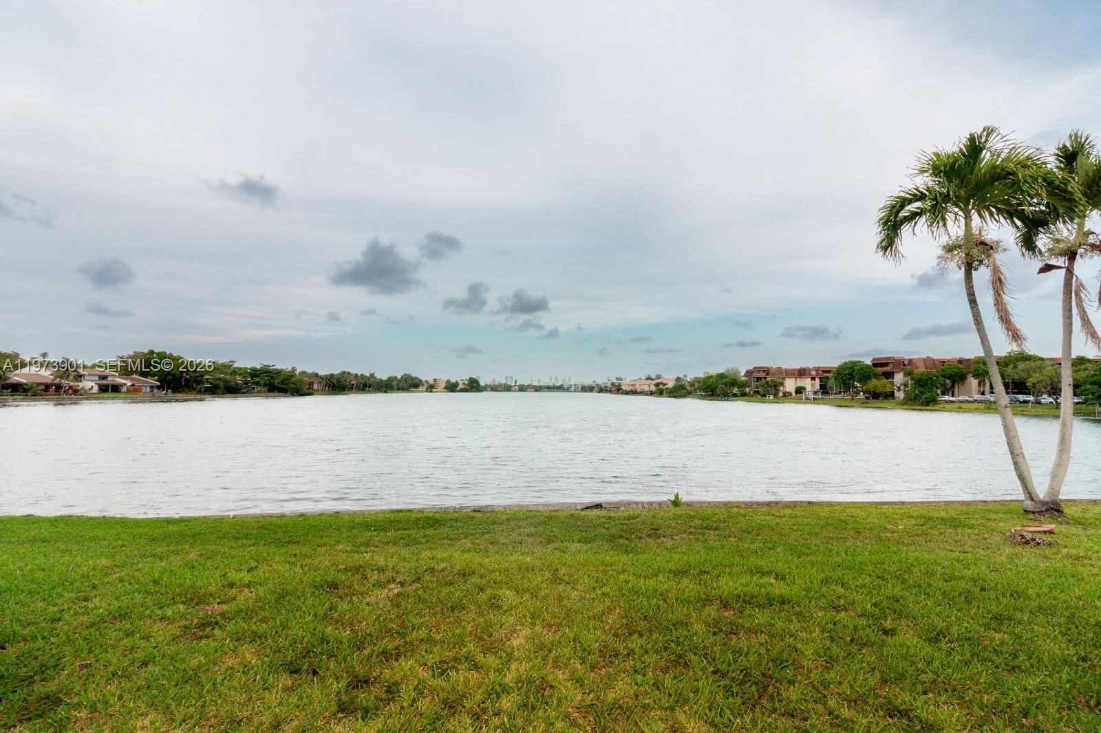 A grassy lawn overlooks a large lake with residential buildings in the distance — 447 NE 195th St # 217, Miami FL 33179, MIAMI, FL