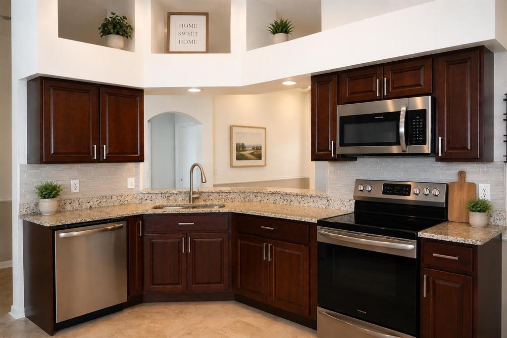 A kitchen features dark wood cabinets, granite countertops, stainless steel appliances, and a tiled backsplash — 14648 CORKWOOD DRIVE, TAMPA, FL