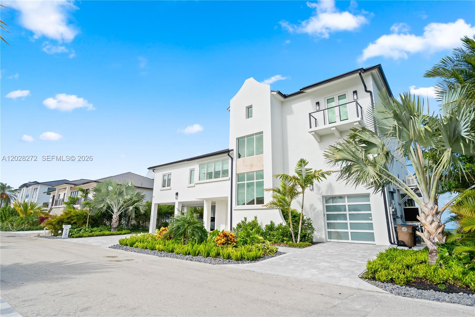 A modern white three-story house features a glass garage door and a balcony under blue skies — 128 Sunrise Drive, Marathon FL 33050, MARATHON, FL