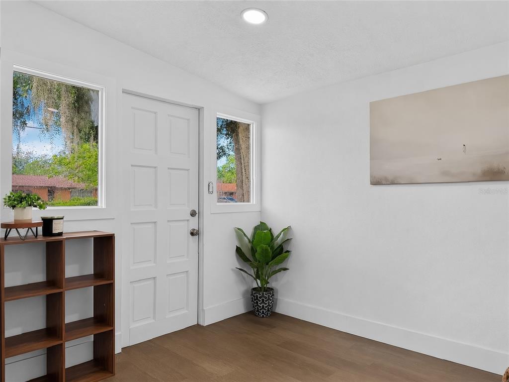 A bright entryway features white walls, wood-look flooring, a white door, and a wooden bookshelf — 3911 LAKE MARGARET DRIVE, ORLANDO, FL