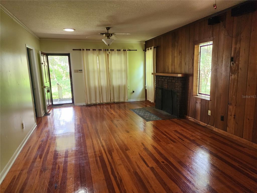 A living room features hardwood floors, wood-paneled walls, a brick fireplace, and a glass door — 1427 NE 10TH STREET, OCALA, FL