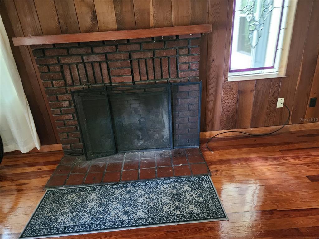 A brick fireplace with a wooden mantel sits in a room with wood-paneled walls — 1427 NE 10TH STREET, OCALA, FL