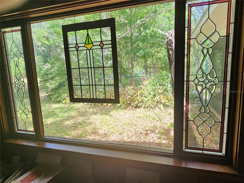 A large window with stained glass accents overlooks a wooded backyard — 1427 NE 10TH STREET, OCALA, FL