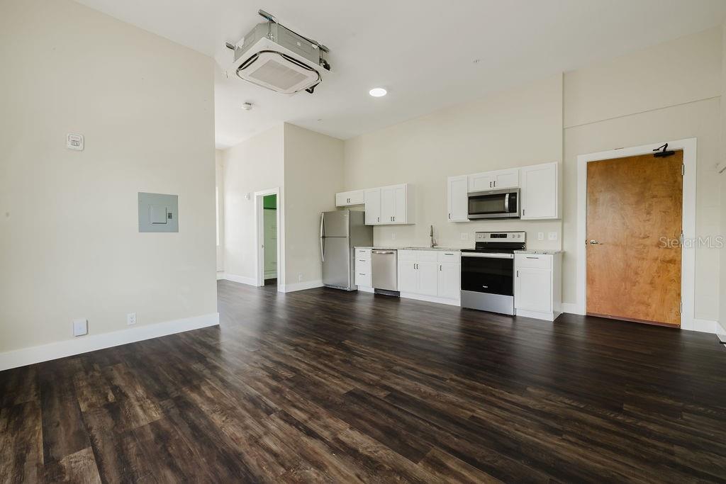 A kitchen with white cabinets and stainless steel appliances opens into a living area — 306 W WISCONSIN AVENUE UNIT 209, DELAND, FL