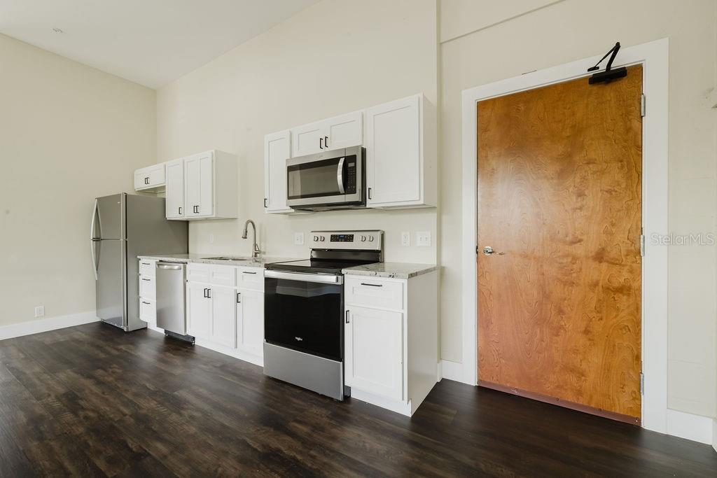 A kitchen features white cabinets, stainless steel appliances, and dark wood-look flooring — 306 W WISCONSIN AVENUE UNIT 209, DELAND, FL