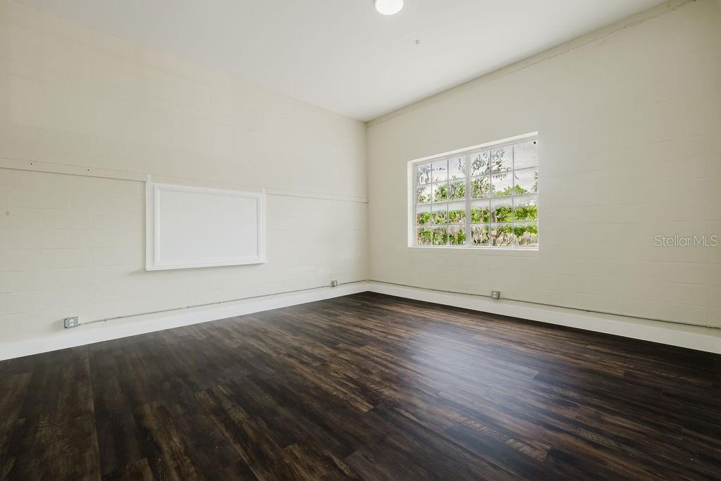 An empty room with light-colored block walls, dark wood-look flooring, and a large window — 306 W WISCONSIN AVENUE UNIT 209, DELAND, FL