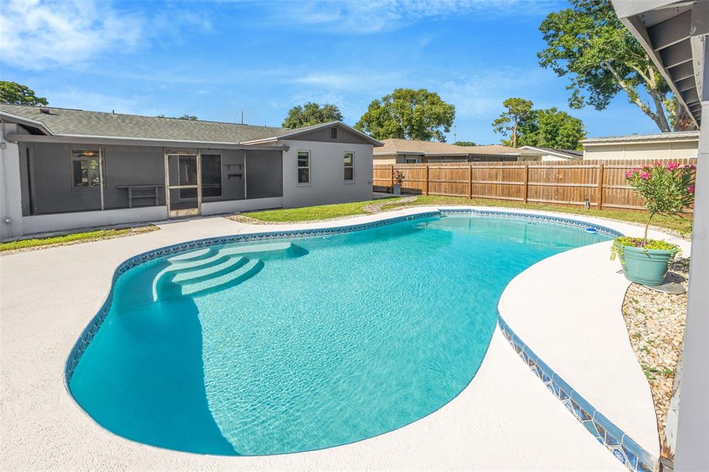 A backyard features a swimming pool with steps, a screened patio, and a wooden fence — 4608 SOUTHBREEZE DRIVE, TAMPA, FL