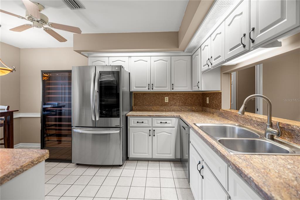 A kitchen features white cabinets, granite countertops, a stainless steel refrigerator, and a wine cooler — 2052 SE 37TH COURT CIRCLE, OCALA, FL