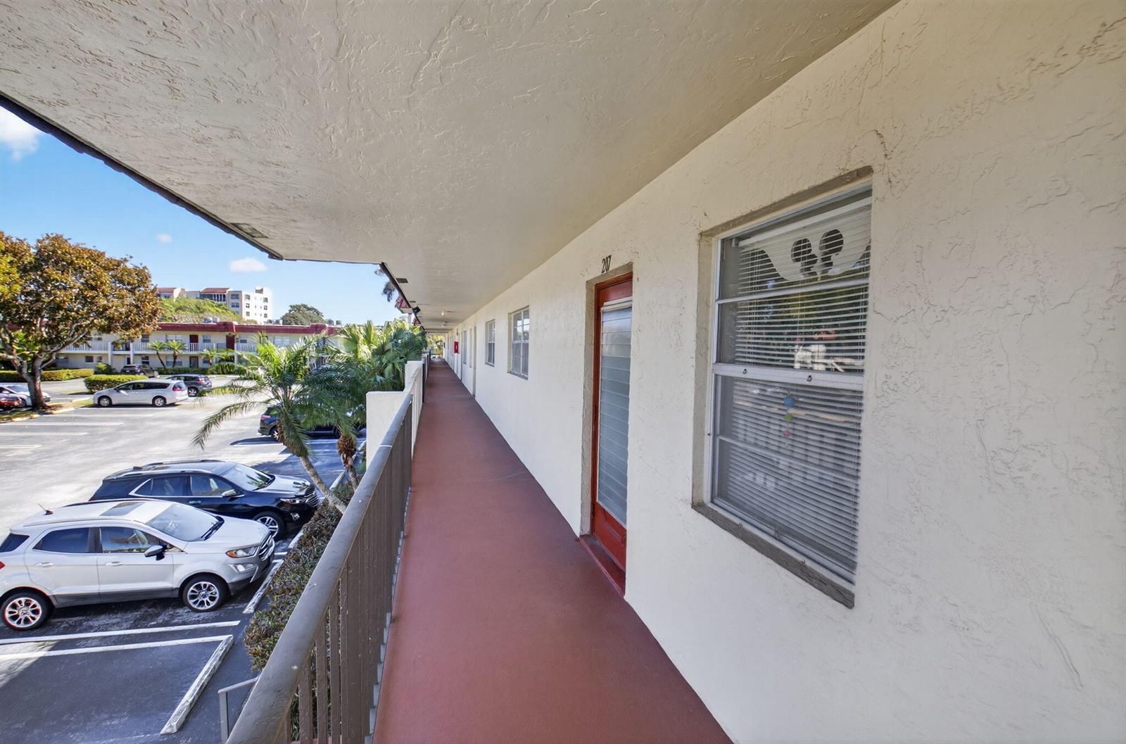 An exterior walkway with a red floor overlooks a parking lot with several cars — 33 Abbey Lane # 207, Delray Beach FL 33446, DELRAY BEACH, FL