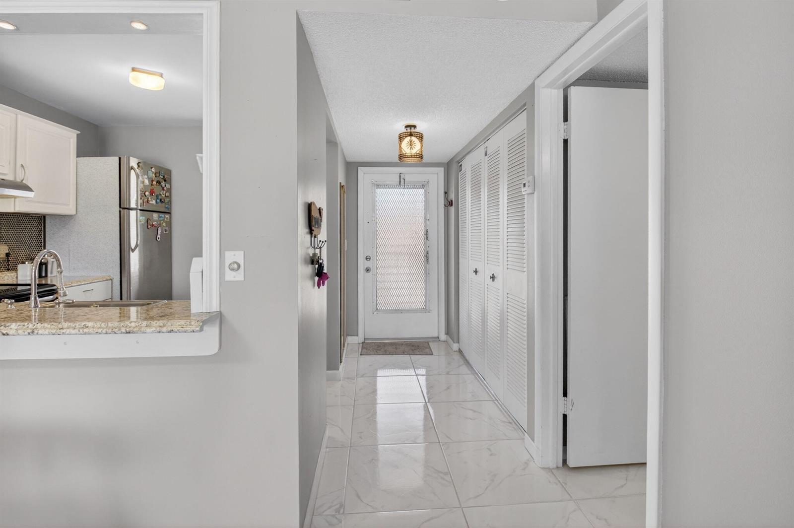 A hallway with white tile floors leads to an exterior door with a screen — 33 Abbey Lane # 207, Delray Beach FL 33446, DELRAY BEACH, FL