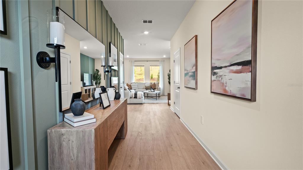 A hallway featuring wood-look flooring, a wooden console table, and wall art leads to a living room — 1901 FIELDSTONE STREET, MINNEOLA, FL