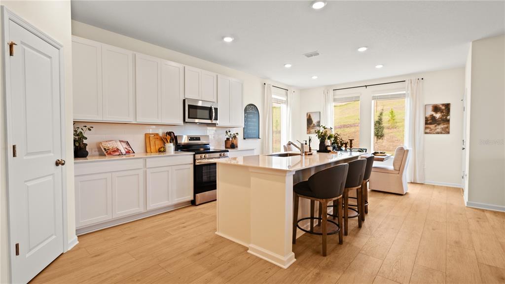A modern kitchen features white cabinetry, a central island with bar seating, and light flooring — 1901 FIELDSTONE STREET, MINNEOLA, FL