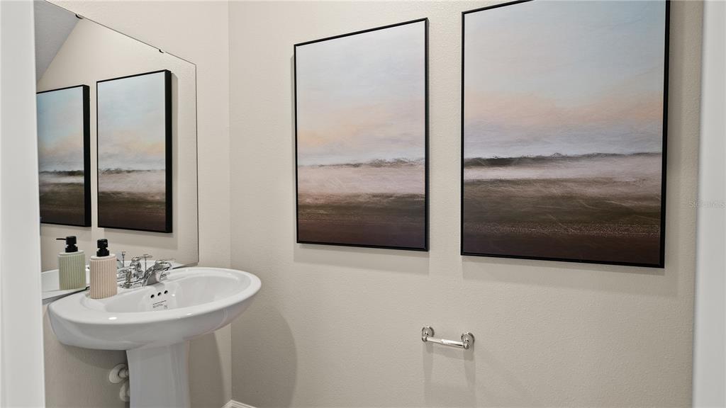 A powder room features a pedestal sink, a wall mirror, and two framed landscape paintings — 1901 FIELDSTONE STREET, MINNEOLA, FL